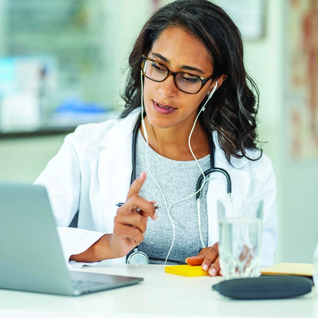 A clinician wearing a headset consults with a patient using a laptop.