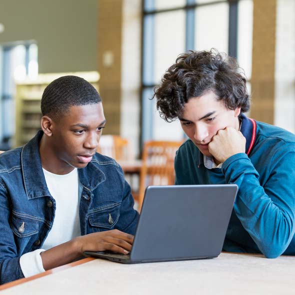 Two teenage boys in library using laptop