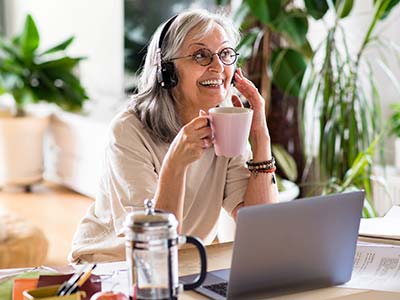 Smiling senior woman with headphones at the table in home office, working