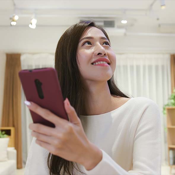 Smiling woman holding phone that she just used to turn lights on in her home.
