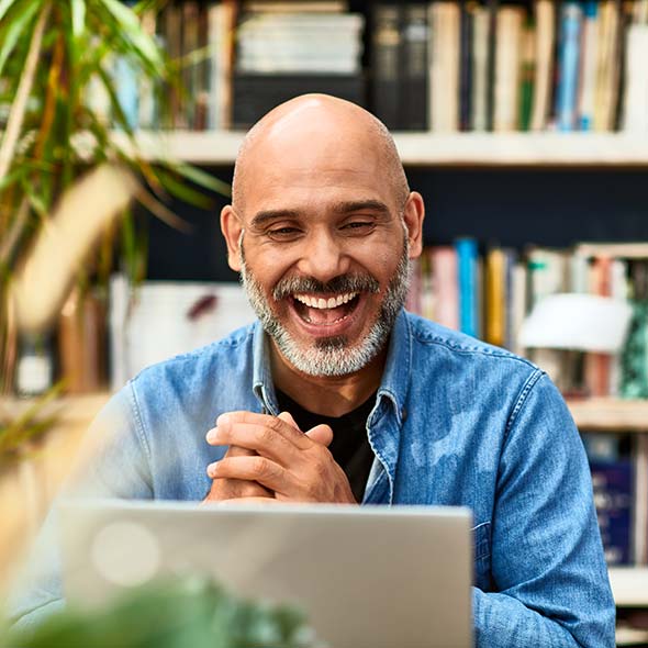 Older man smiling at laptop in front of bookcase