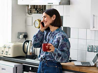 Cheerful woman on phone in kitchen drinking coffee