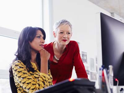 Mature business woman with younger employee both looking at a laptop
