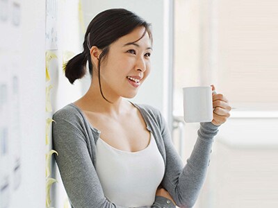 Woman holding a cup of coffee and standing in front of a wall