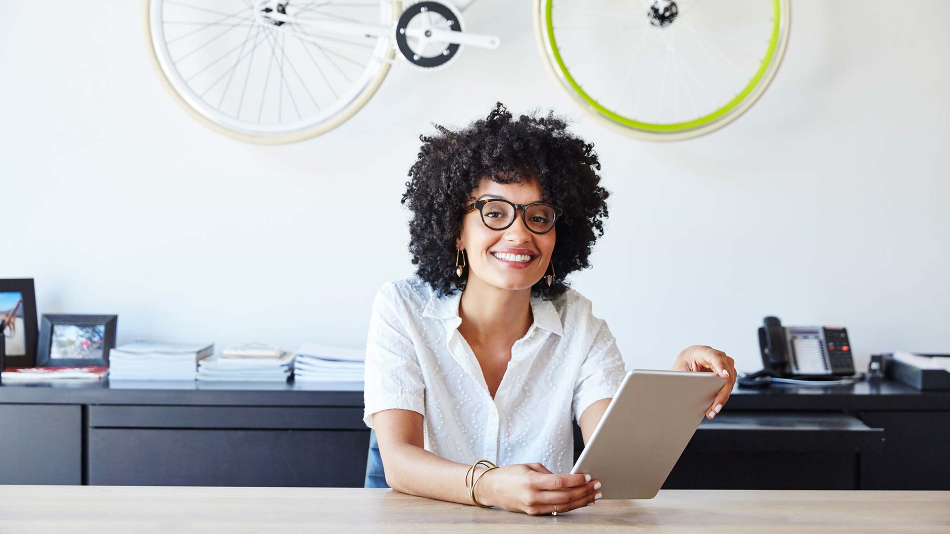 Girl with glasses on holding a laptop with a bicycle behind her