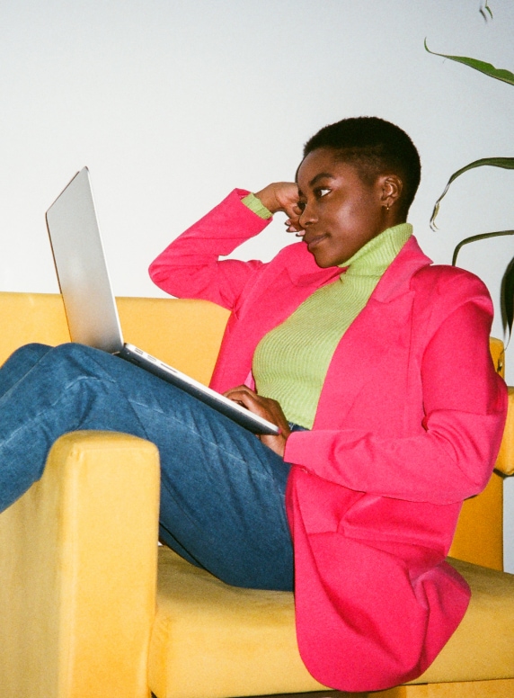 Woman sitting sideways in armchair working on her laptop.