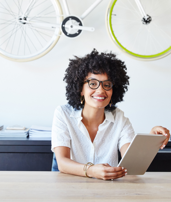 Woman sat at a desk, smiling, holding a tablet.