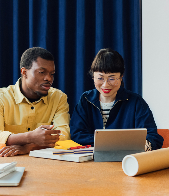 Man and woman at desk looking at tablet.