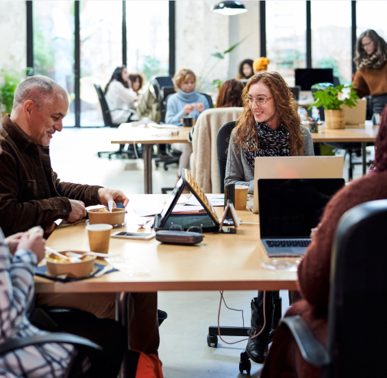 Workers at desks in open office, eating and talking